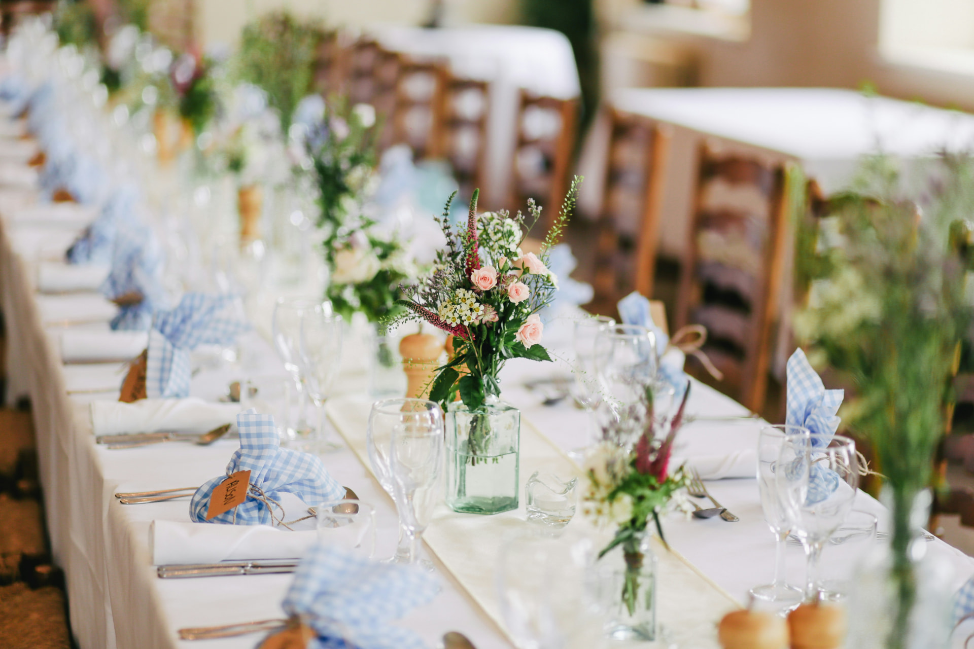 Elegant wedding reception table with blue gingham napkins, floral centerpieces, and crystal glassware